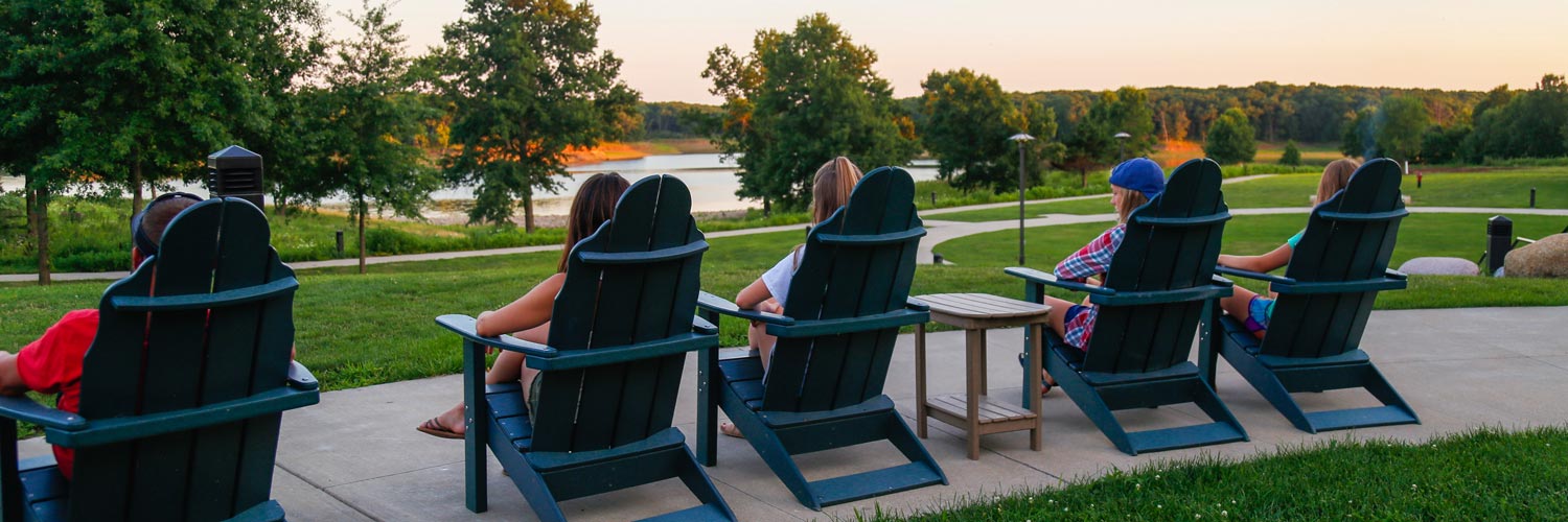 People relaxing in adirondack chairs at Honey Creek Resort looking out at Rathbun Lake