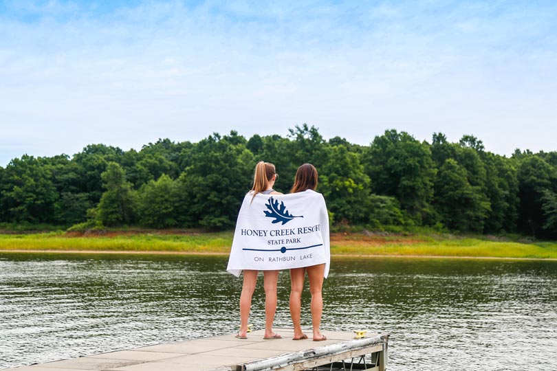 Two girls hold Honey Creek Resort towels on the marina docks at Rathbun Lake